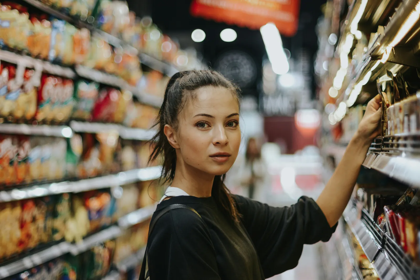 Young woman reaching for a product on a supermarket shelf