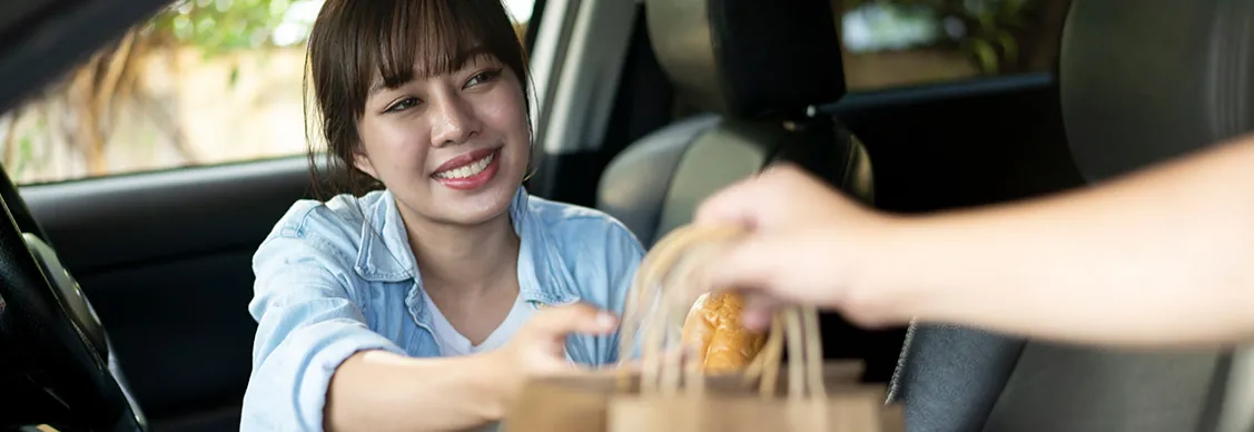 Woman in a car collecting a paper bag of shopping from a store worker